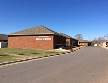 A brick building with a sign that says "The Meadows STORM SHELTER".